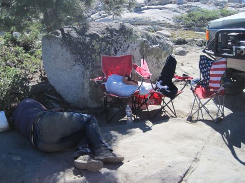 1989 Ford Bronco - A person sleeps on the ground next to camping chairs and a 1989 Ford Bronco.