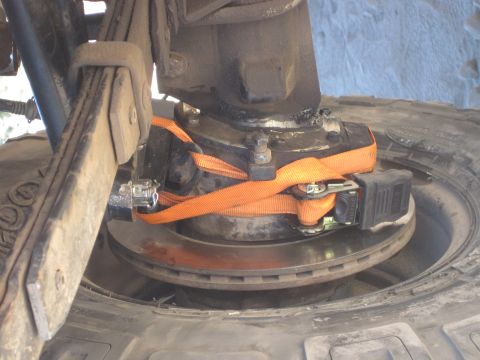 1989 Ford Bronco - A close-up view of a vehicle's suspension and brake components, held in place by orange ratchet straps.
