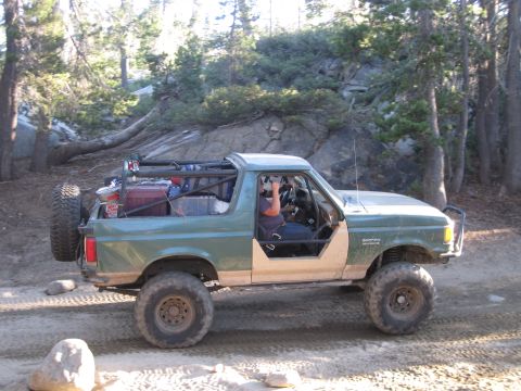 1989 Ford Bronco - Modified Ford Bronco navigates a dirt path in a wooded, rocky area.