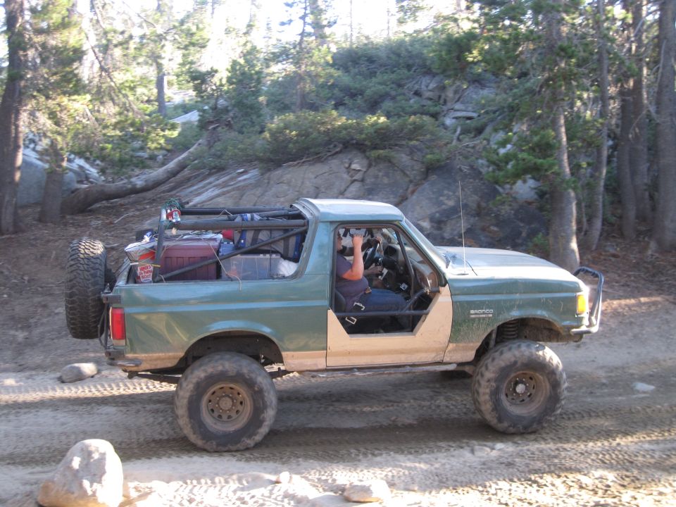 Green Ford Bronco with off-road modifications, spare tire on back, driving on dirt trail