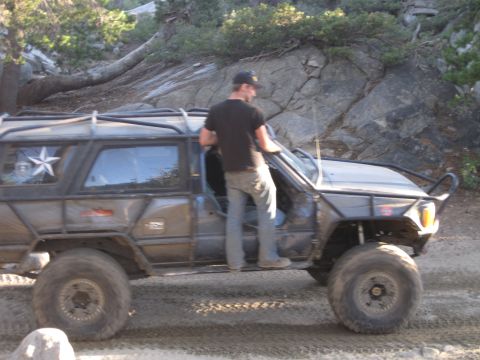 1989 Ford Bronco - Modified SUV with a prominent roll cage and oversized tires sits on a dirt road.