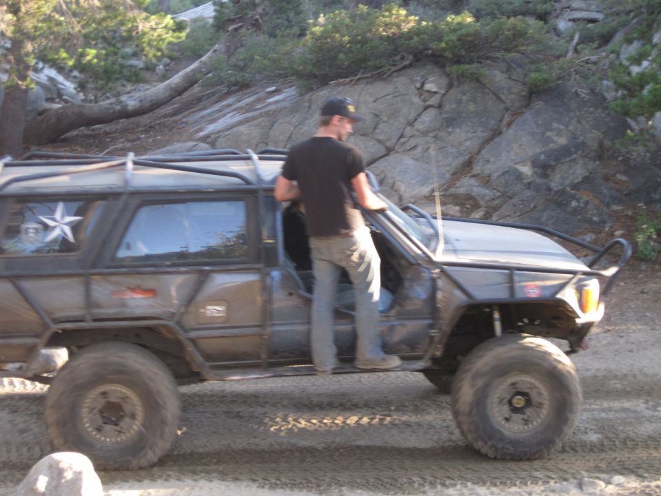 Modified SUV with roll cage and large tires, driver entering. Gray exterior