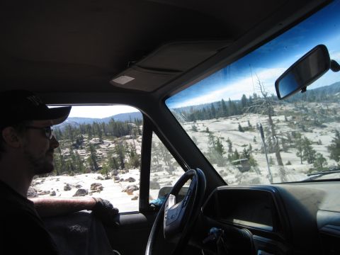 1989 Ford Bronco - View from inside a truck cab shows a man looking out at a , mountainous landscape with scattered pine trees.