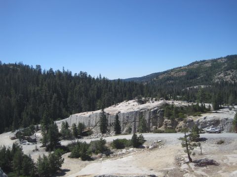 1989 Ford Bronco - A scenic view of a mountain road surrounded by dense pine forests and rocky terrain.