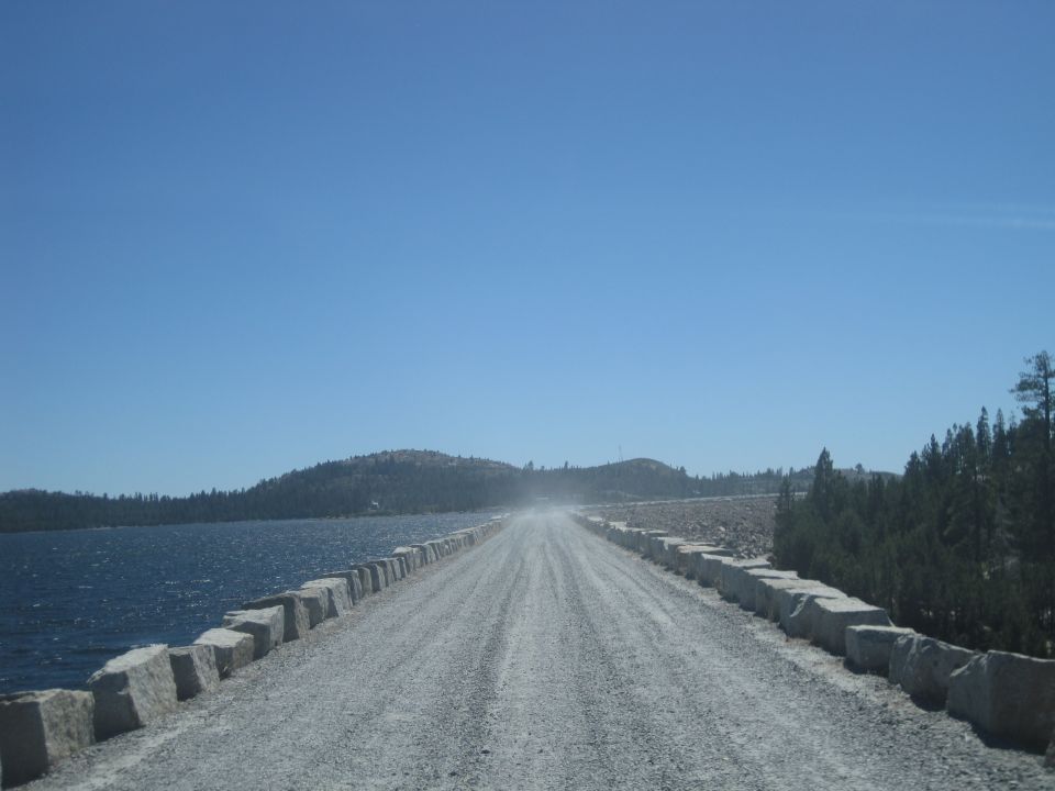 Gravel road with stone barriers next to a body of water under a clear blue sky