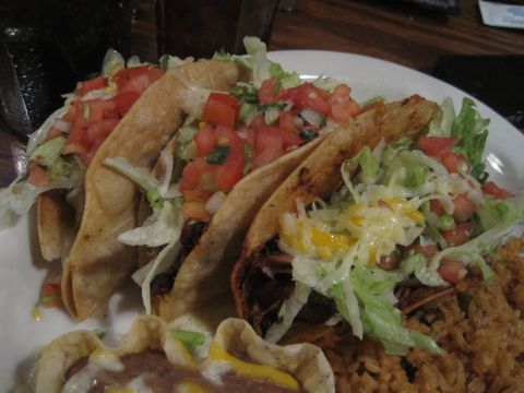 1989 Ford Bronco - A plate of three tacos, generously topped with shredded lettuce, diced tomatoes, and cheese, accompanied by a side of rice and beans.