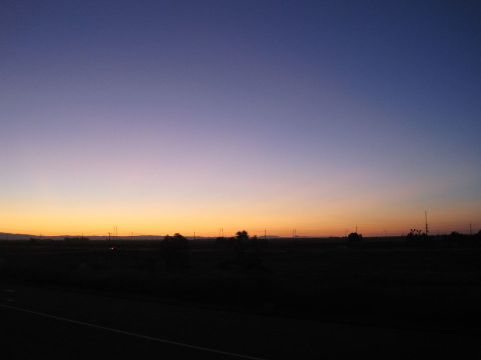 Sunset sky with purple and orange gradients over a dark, silhouetted rural landscape with power lines