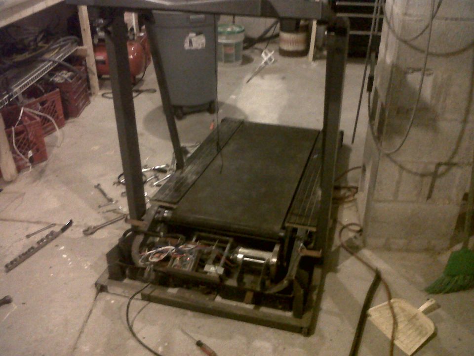 Partially disassembled treadmill with exposed motor and roller on a basement floor