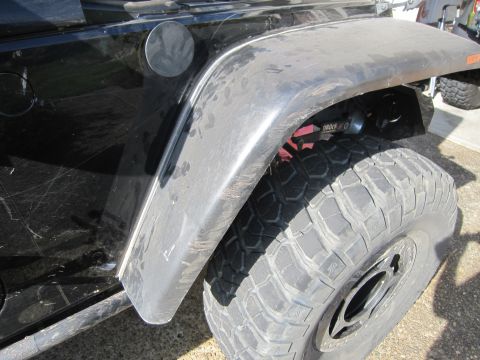 2008 Jeep Wrangler - The side of a black Jeep Wrangler shows its fender, large off-road tire, and a gas cap.