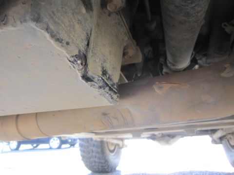 2008 Jeep Wrangler - Close-up view of the underbody of a vehicle, showing a damaged metal plate and exhaust pipe.