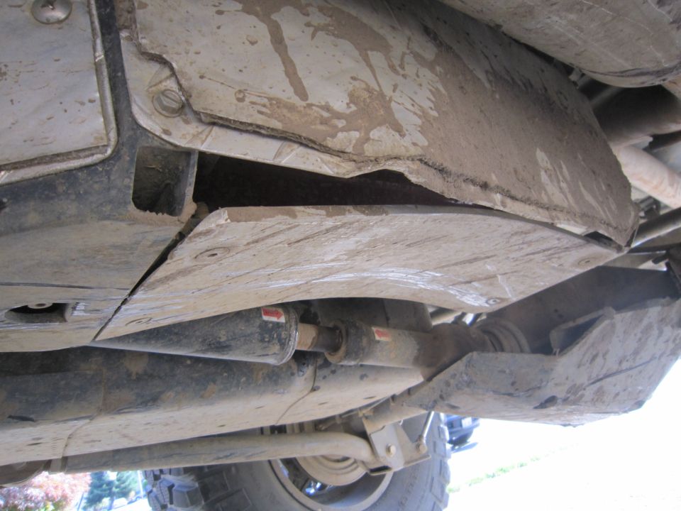 Underside of a vehicle showing skid plates and drive shaft. One skid plate is bent