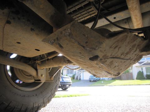 2008 Jeep Wrangler - The underside of a vehicle shows a heavily rusted skid plate and suspension parts, with other vehicles visible in the background.