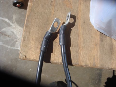 1989 Ford Bronco - Two black battery cables with metal ring terminals lie on a wooden surface.