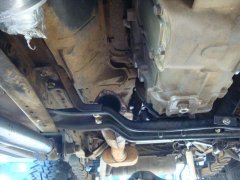 1989 Ford Bronco - The underside of a vehicle reveals its transmission and exhaust components, with a focus on the drivetrain.