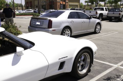 2006 Cadillac STS - Two cars parked in a lot, with a man standing near a bush and other vehicles in the background.