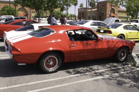2006 Cadillac STS - A red 1970s muscle car with white racing stripes is parked in a lot next to other vehicles.