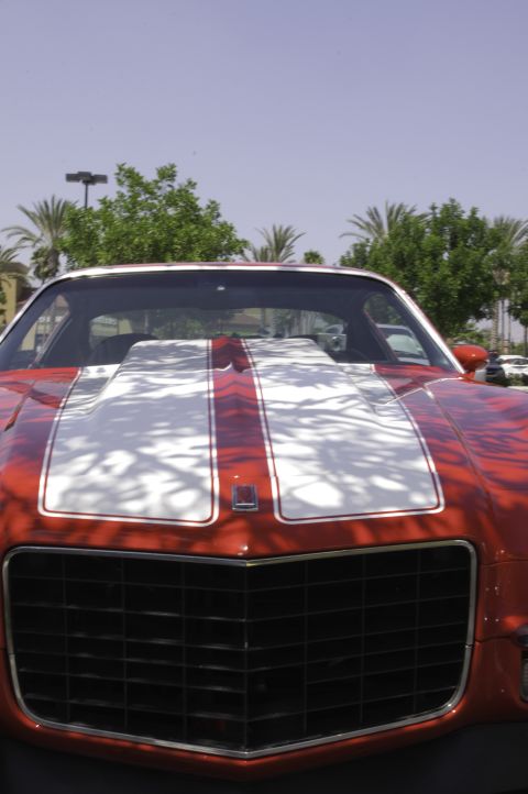 2006 Cadillac STS - A red muscle car with white racing stripes on the hood is parked outdoors on a sunny day.