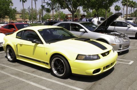 2006 Cadillac STS - A yellow Ford Mustang is parked in a lot with other vehicles, one with its hood open.