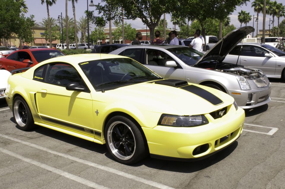 Yellow Ford Mustang with black racing stripes and black rims parked in a lot