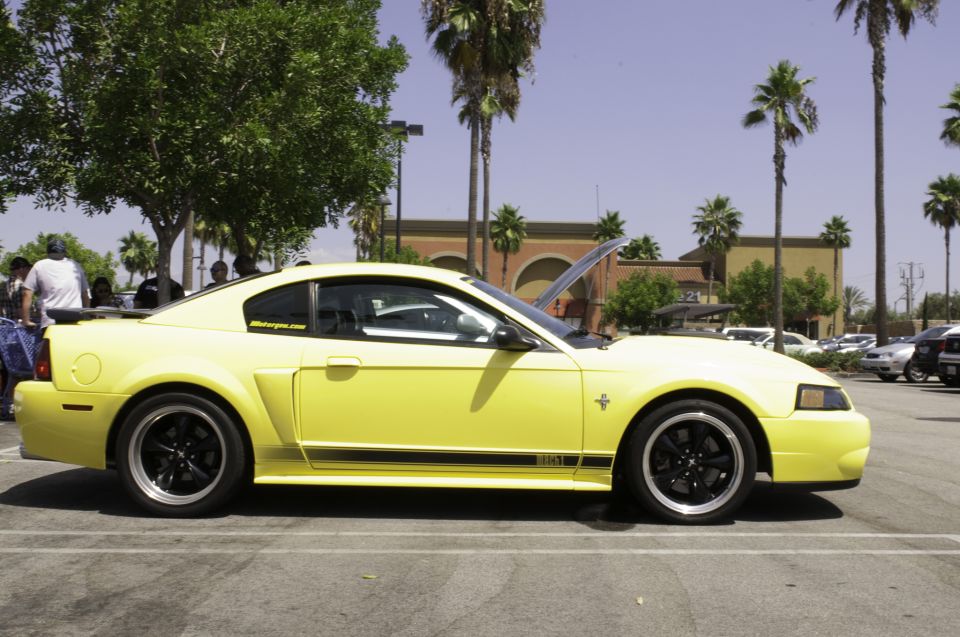 Yellow New Edge Ford Mustang side profile with black Mach 1 rocker stripe and hood open at a car show