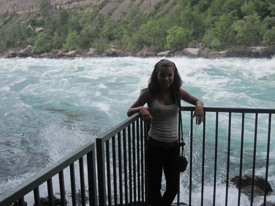 Woman in tank top and jeans leans on railing by raging river