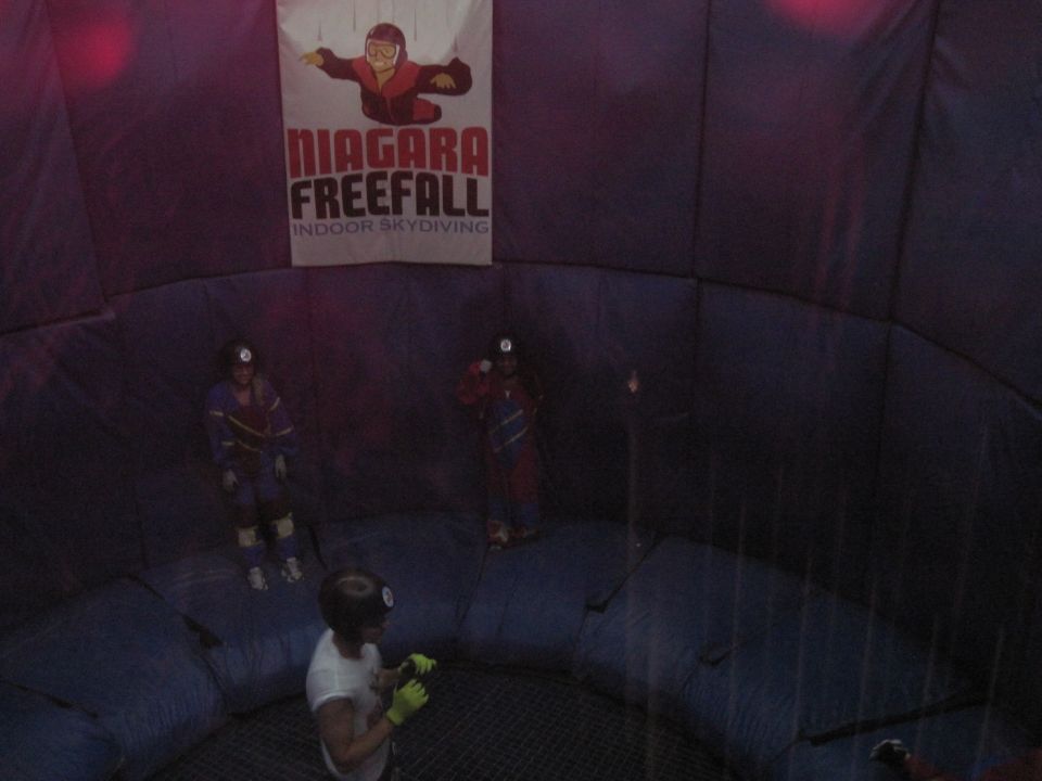 People in jumpsuits inside a wind tunnel with a 'Niagara Freefall' banner