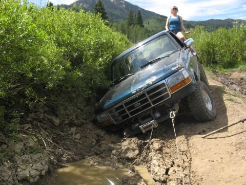 1995 Ford Bronco - A blue Ford Bronco is stuck in a muddy ditch, with a woman sitting on the roof.