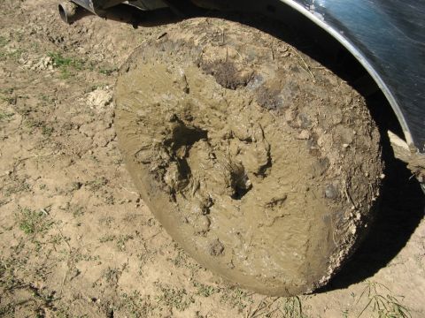 1995 Ford Bronco - A vehicle's tire is deeply embedded in thick mud.