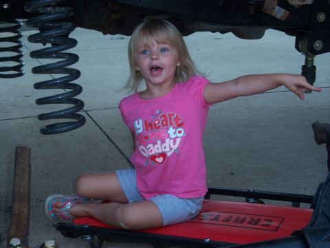 1996 Ford Bronco - A young girl sits on a creeper, looking surprised and pointing while underneath a vehicle.