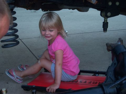 1996 Ford Bronco - A young girl sits on a creeper beneath a vehicle, possibly during maintenance or modification.