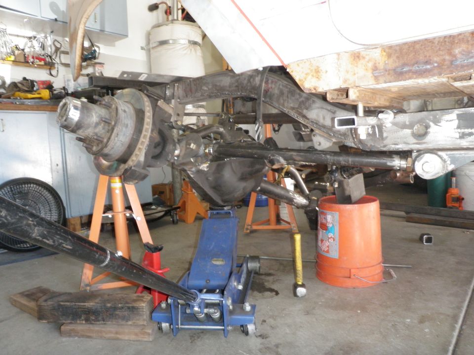 Vehicle chassis on jack stands with front suspension and differential visible, undergoing repair