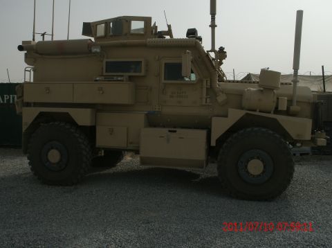 1988 Ford Bronco - A side view of a tan US Navy military truck parked on a gravel surface.