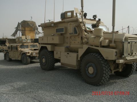 1988 Ford Bronco - Two military trucks are parked on a gravel lot under a clear sky.