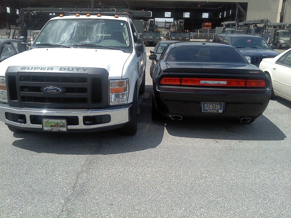 White Ford Super Duty truck parked beside a black Dodge Challenger in a lot