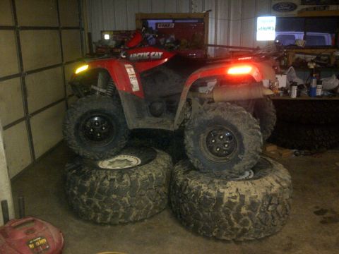 1994 Ford F-150 - An Arctic Cat ATV is elevated on a stack of four large tires inside a garage.