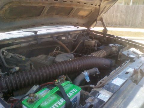 1995 Ford Bronco - The engine bay of a vehicle shows a large air intake hose and a green Interstate battery, with no clear year identification visible.