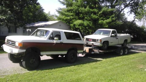 1989 Ford Bronco - A 1989 Ford Bronco is seen towing a GMC pickup truck on a trailer in a residential setting.