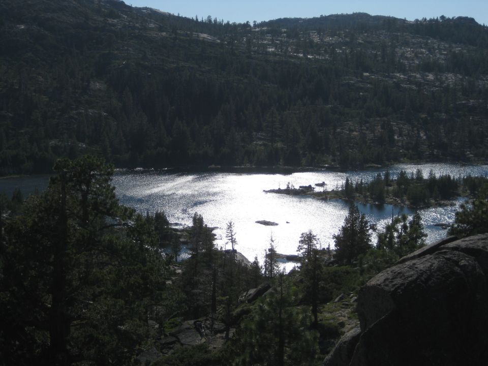 Lake reflecting sunlight, surrounded by pine trees and mountains