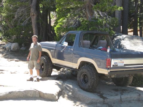 1986 Ford Bronco - A man stands next to a lifted 1986 Ford Bronco navigating rocky terrain.