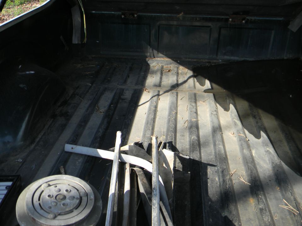 Truck bed interior with some metal parts and a round component. Sunlight casts shadows