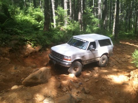 2005 Jeep Wrangler - A white SUV navigates a challenging rocky trail through a dense forest.