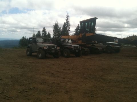 2005 Jeep Wrangler - Two Jeep Wranglers and a CAT construction vehicle are parked on a dirt lot under a cloudy sky.