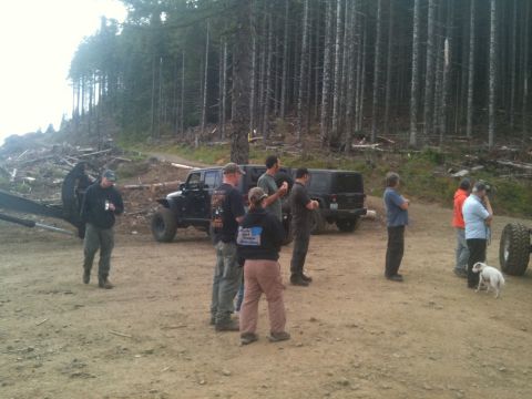 2005 Jeep Wrangler - People gather around Jeeps in a clearing surrounded by tall trees and evidence of logging.