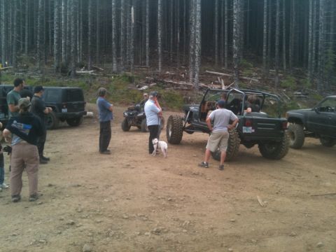 2005 Jeep Wrangler - Several off-road vehicles are gathered in a wooded area with a dirt ground.
