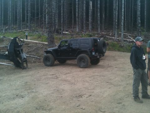 2005 Jeep Wrangler - A black Jeep Wrangler Unlimited is parked in a wooded area, with logging equipment nearby.