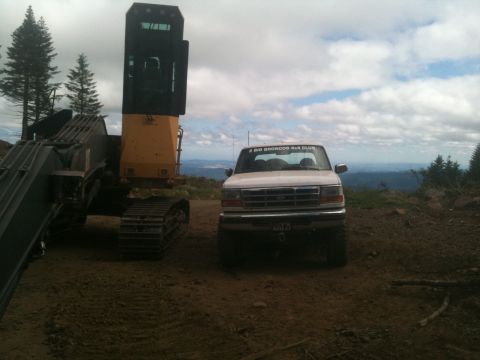 2005 Jeep Wrangler - A white Ford Bronco is parked on a dirt road next to a large yellow excavator, with a scenic view of rolling hills under a cloudy sky.