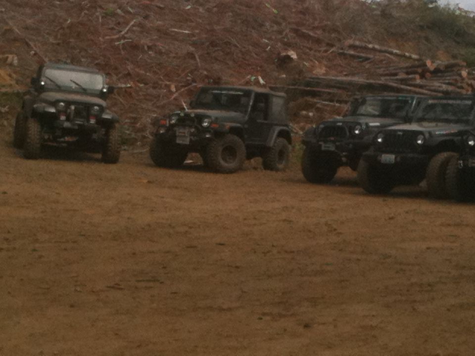 Four Jeep Wranglers parked on a dirt lot with a wooded hillside in the background