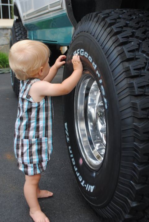 1994 Ford Bronco - A toddler inspects the massive tire of a 1994 Ford Bronco, highlighting the vehicle's imposing size.