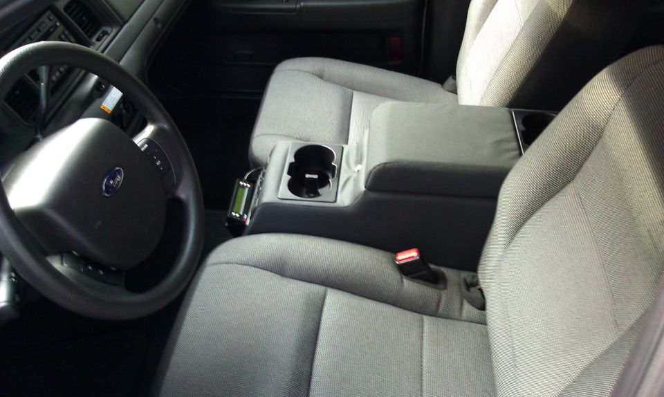 Gray cloth front seats and steering wheel inside a Ford Crown Victoria, with center armrest and cup holders