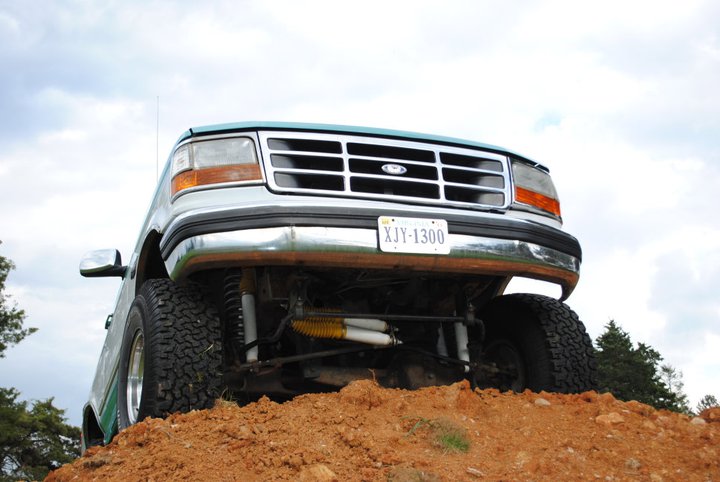 Front view of a 1992 Ford F-150 pickup truck with lifted suspension, driving over dirt mounds